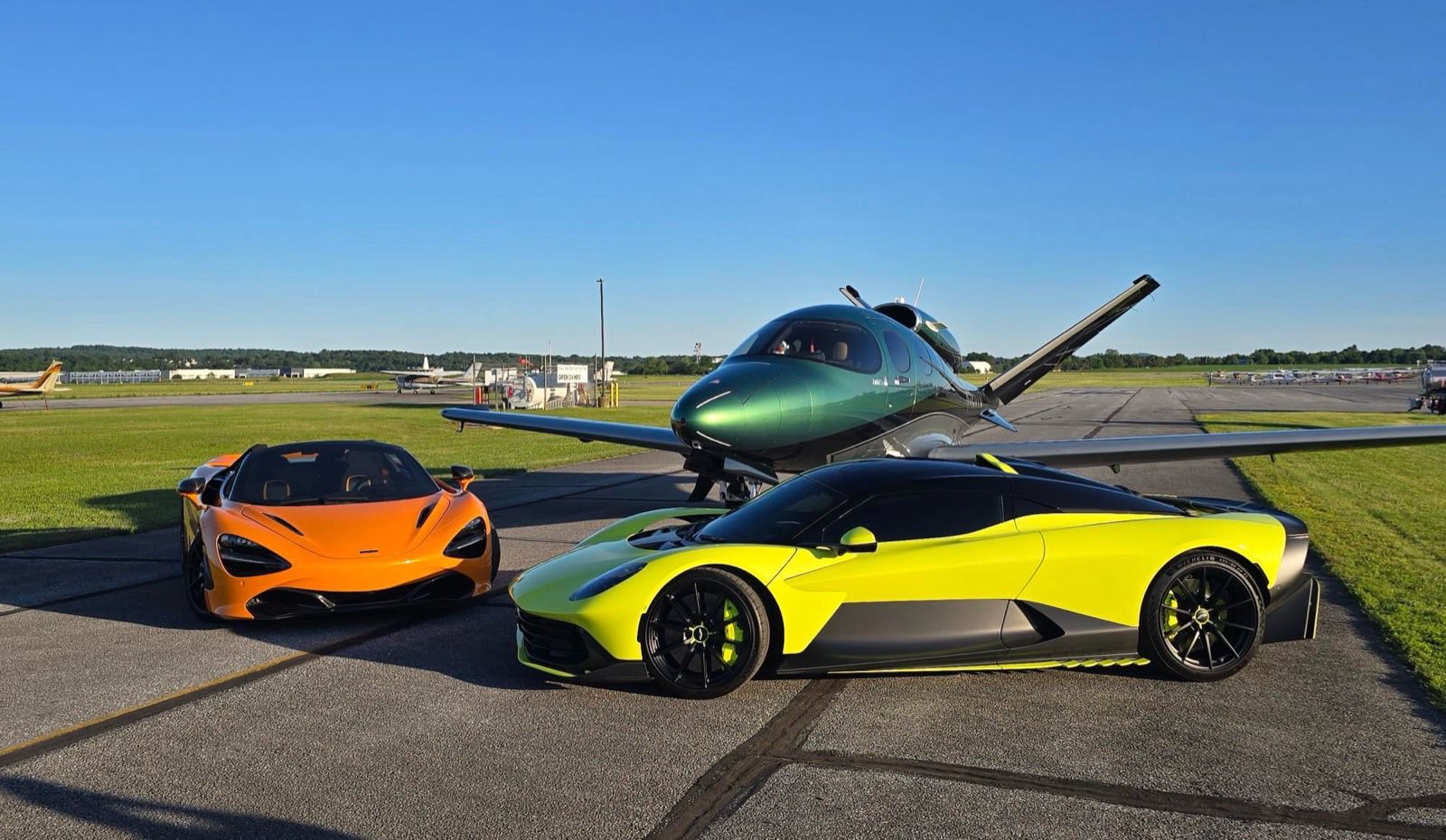 Aston Martin Valhalla and McLaren 720S Spider parked beside a private jet at sunset